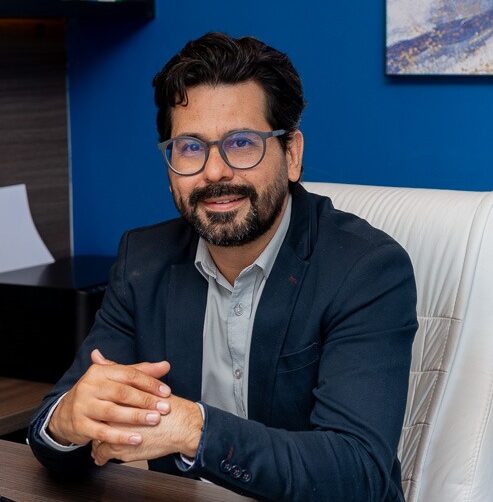 Sentado na cadeira branca com mãos na mesa do consultório 1